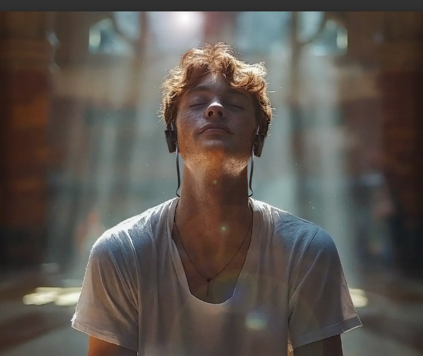 A young man sits in a sun beam, eyes closed, relaxing with guided box breathing while wearing Emotiv Brainwear EEG headphones