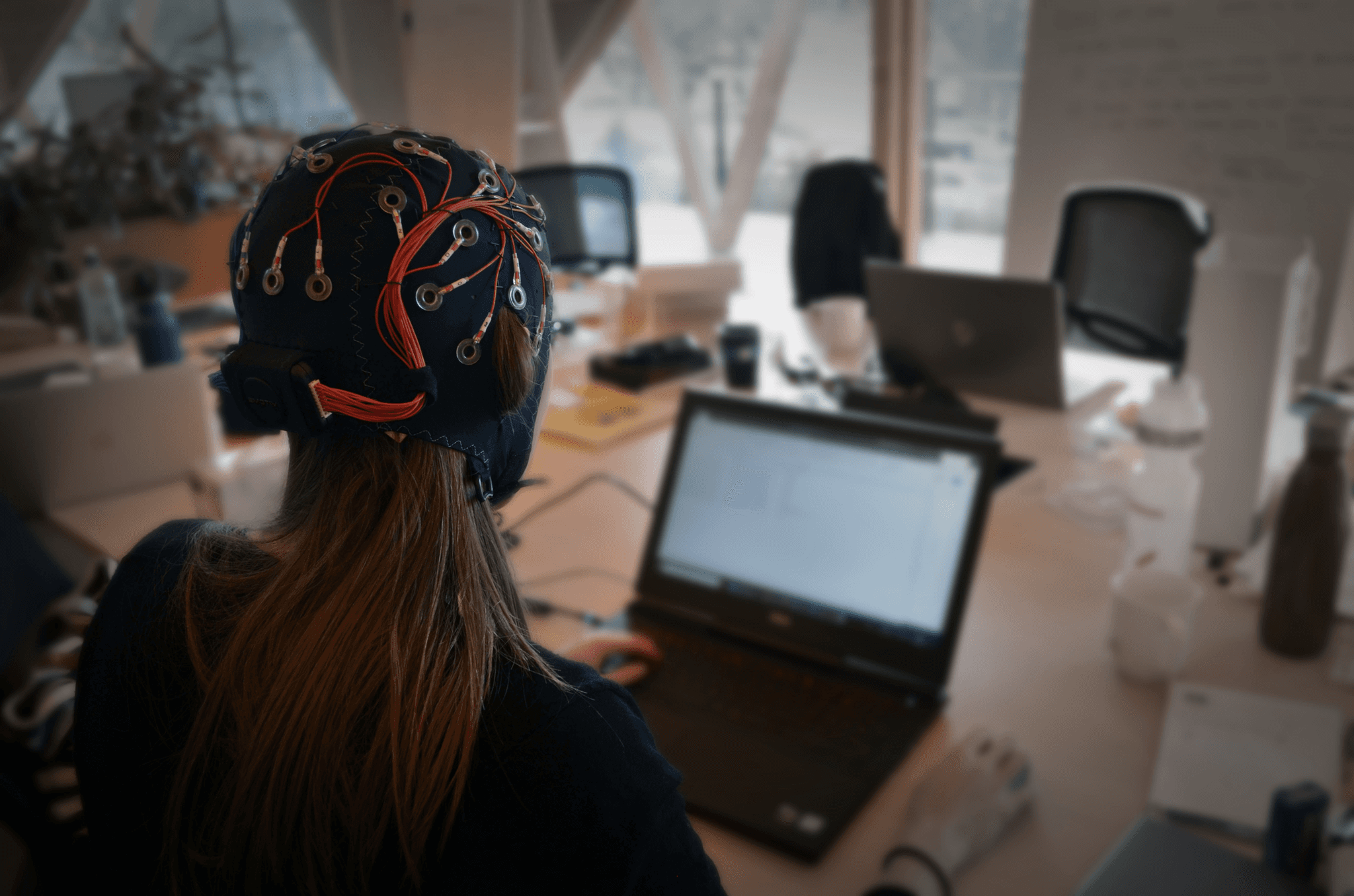 A person wearing an Emotiv EEG cap while working at a laptop in an open office